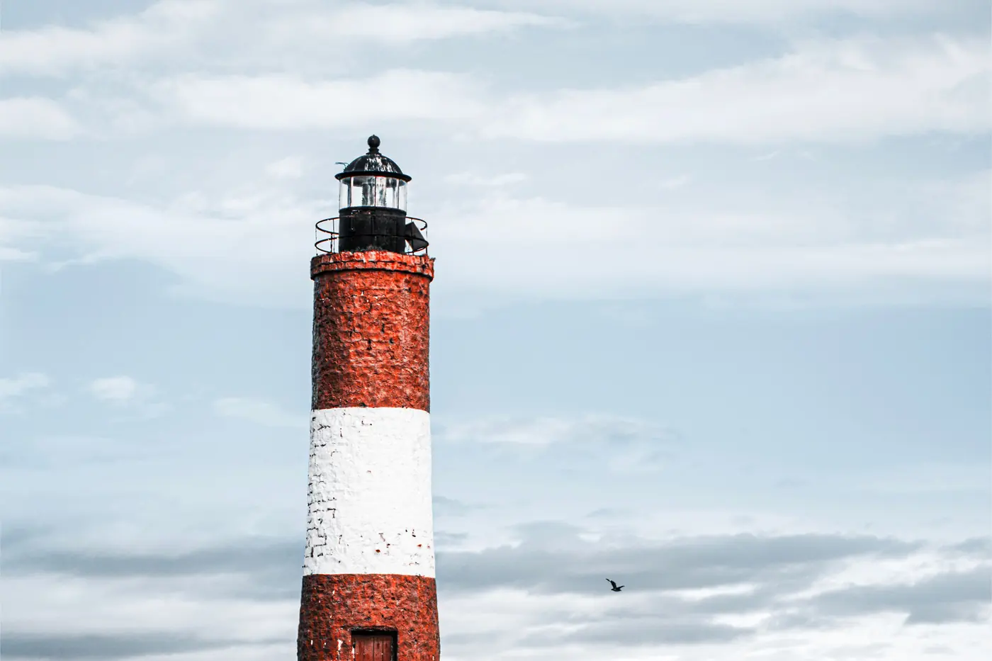 A red and white lighthouse on a rocky headland, mountains behind it.